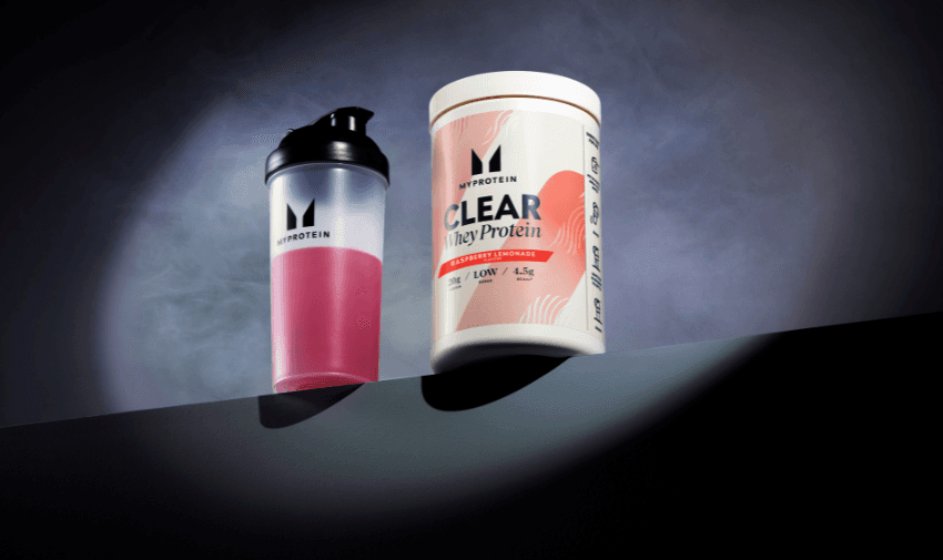 MyProtein shaker with pink liquid and Clear Whey Protein tub in Raspberry Lemonade, set against a smoky backdrop. Includes Shopping Discounts for Disabled People and Mobility Discounts.