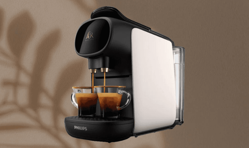 A modern L’OR coffee machine brews two cups of espresso simultaneously. The machine has a sleek, black and white design and is set against a plain, beige background with a shadow of a plant.