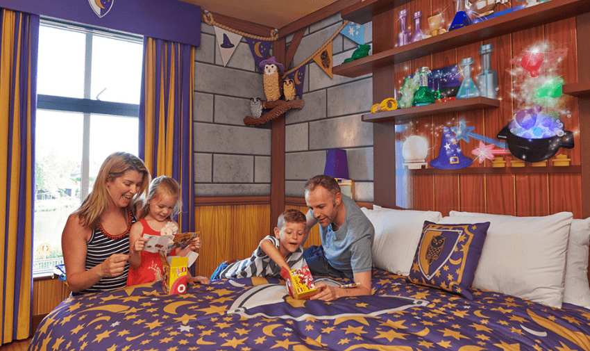 A family spending time together in a wizard-themed hotel room, surrounded by magical decorations like potions, spellbooks, and star-patterned bedding.