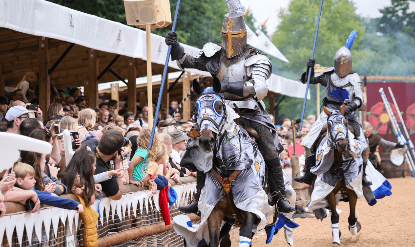 A thrilling jousting event at Warwick Castle, featuring knights in armour on horseback, cheered on by a large crowd. Includes Theme Park Discounts for Disabled Visitors and Free Carer Tickets UK.