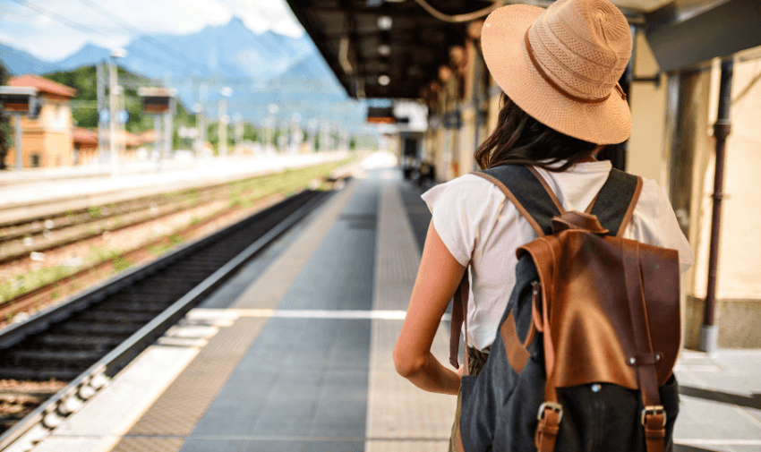 A solo traveller wearing a hat and backpack, standing on a quiet train station platform with mountain views in the background. Promoting TrainPal and Purpl’s disabled travel discounts, offering affordable and accessible rail travel options for UK travellers.