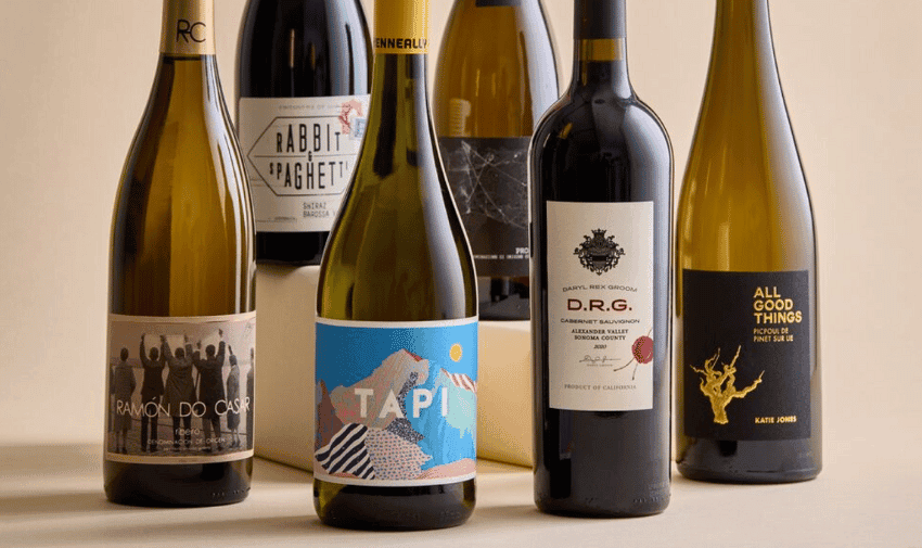 A selection of six wine bottles with various colorful labels is displayed against a beige background. The labels include different designs and text, such as "Rabbit & Spaghetti," "Ramón do Casar," "Tapi," "D.R.G.," and "All Good Things.