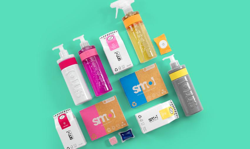 Flat lay of Smol's eco-friendly home care products, including detergents, sprays, and cleaning tablets in vibrant packaging, set against a teal background.