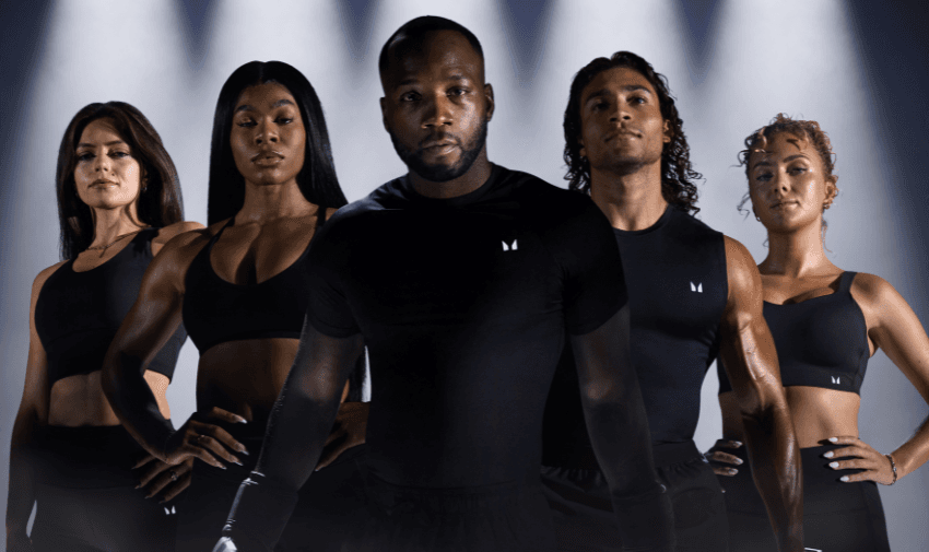 A diverse group of athletes in MyProtein activewear standing confidently under dramatic lighting. Highlights Shopping Discounts for Disabled People and Fitness Apparel Discounts.