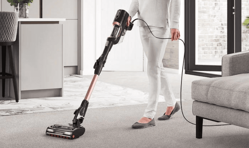 A person vacuuming with a Shark Anti Hair Wrap Corded Stick Pet Vacuum in Rose Gold