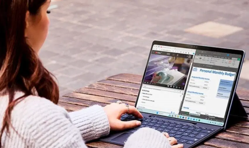 Person using a laptop outdoors, multitasking with a budgeting spreadsheet and online video. High-performance laptop for productivity and entertainment. Disabled discounts on top tech and computing devices.