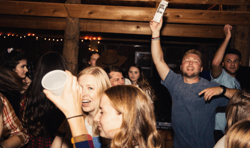 A group of friends clinking glasses filled with drinks in a lively bar setting, showcasing The Bottle Club. Highlighting Purpl's exclusive discounts on beverages and social experiences for disabled people in the UK.