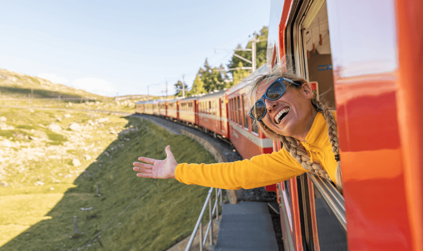 A cheerful traveller leaning out of a scenic red train window, enjoying the journey through lush landscapes. Highlighting TrainPal and Purpl's exclusive disabled travel discounts, making accessible and affordable train journeys possible across the UK.