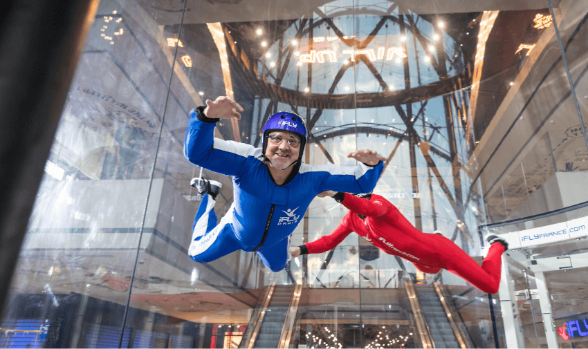 A person in a blue jumpsuit flying inside a vertical wind tunnel at iFLY, guided by an instructor in red. Highlighting Purpl's exclusive disabled travel discounts, offering unique and accessible adventure activities in the UK.