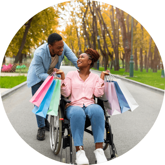 Happy couple: man pushes woman in wheelchair with shopping bags