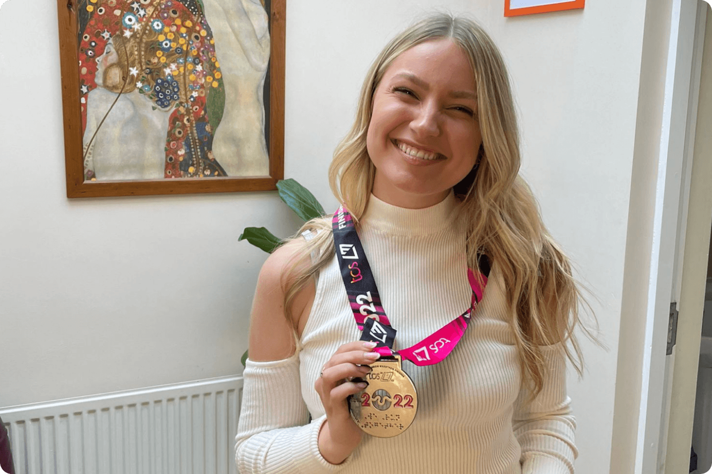 Photo of Amy smiling and holding a 2022 medal that she has around her neck.