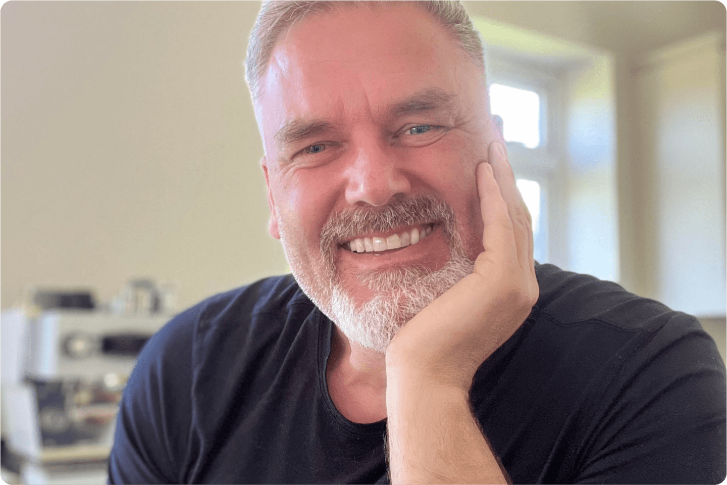 Photo of Gavin smiling at the camera, he has grey hair and beard. He is wearing a navy top and looks very happy.