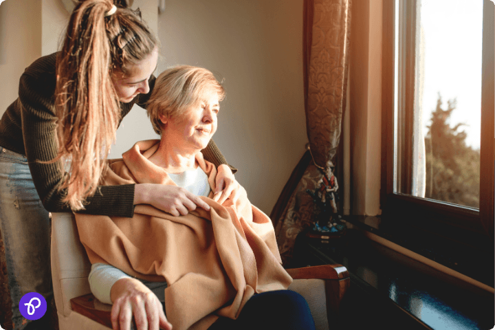 A young woman comforting an elderly lady by the window, illustrating community support for disabilities.