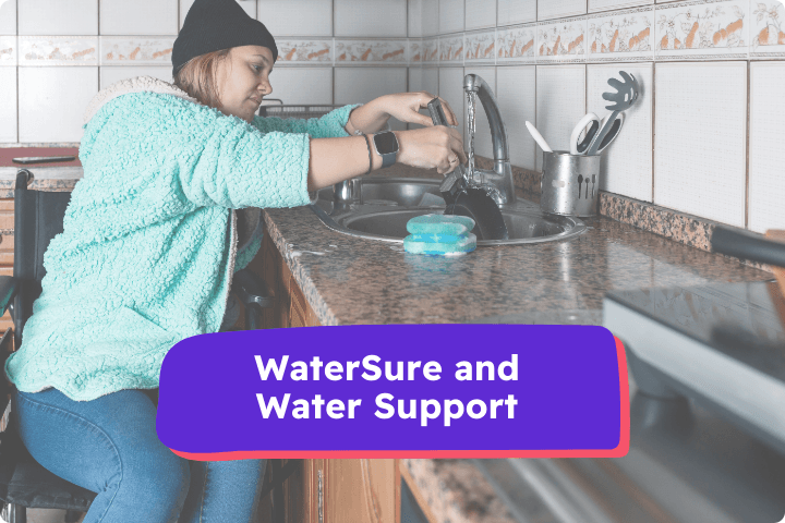 A woman is a wheelchair user and is washing the pots in a kitchen, she is wearing a turquoise jumper and and hat