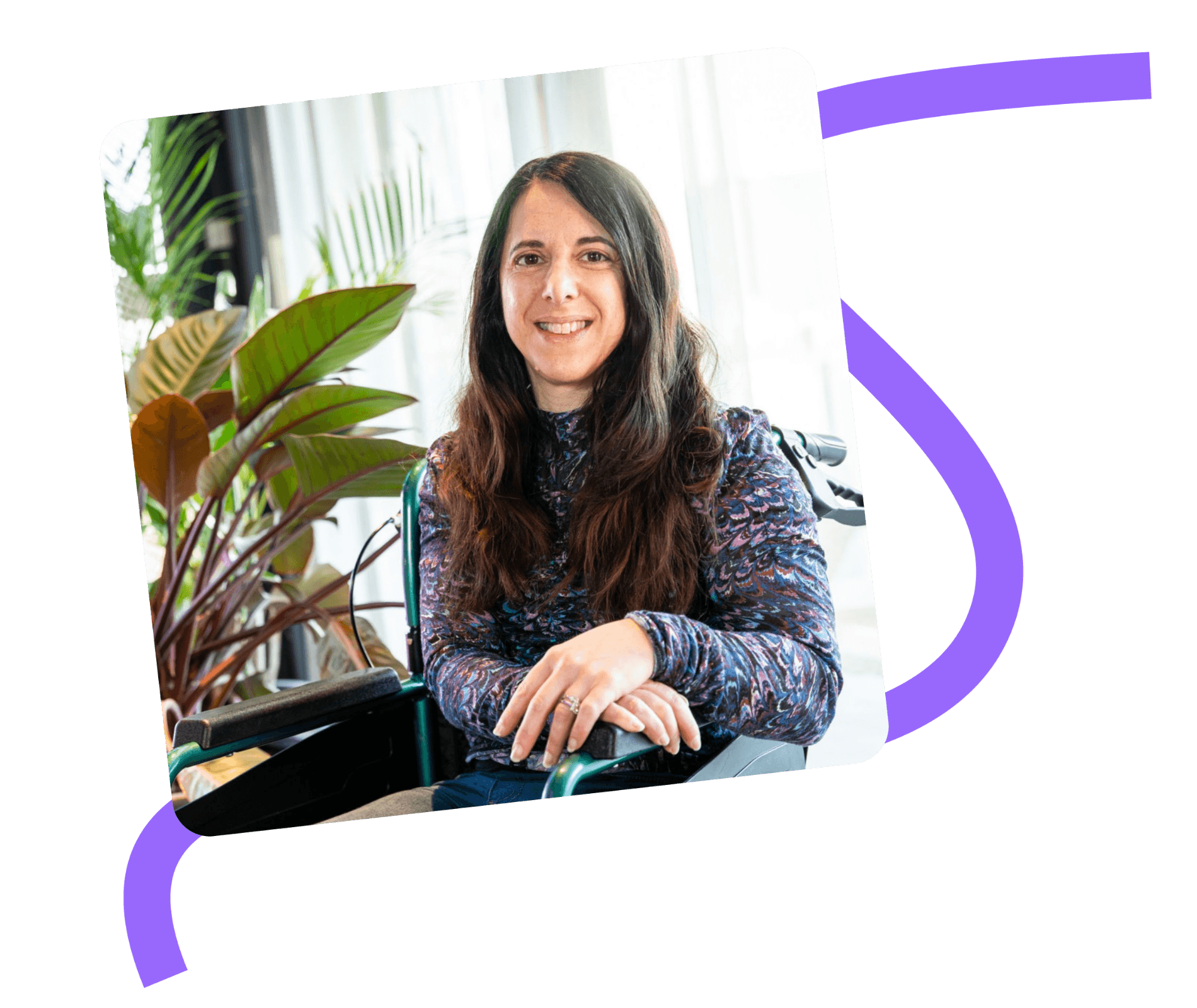 Georgina Colman founder of Purpl Disabled Discounts, is a white woman with long dark hair, she is sat in a wheelchair in a hotel lobby by a large plant.