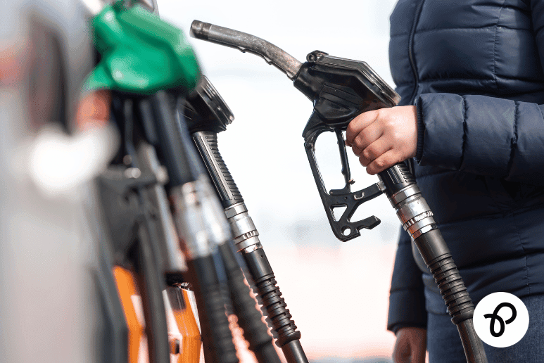Person holding a petrol pump at a fuel station, showing everyday travel costs and fuel price comparison for disabled people and those with long-term health conditions in the UK.