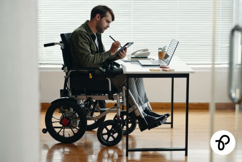 Wheelchair user working at a desk while managing higher living costs due to disability and long term health conditions in the UK using Purpl discounts.